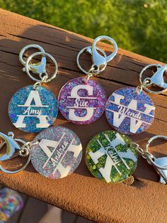 six keychains with different designs on them sitting on a wooden bench in the sun