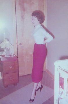 an old photo of a woman standing in a room with a crib and dresser