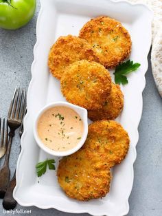 three fried crab cakes on a white platter with a small bowl of dipping sauce