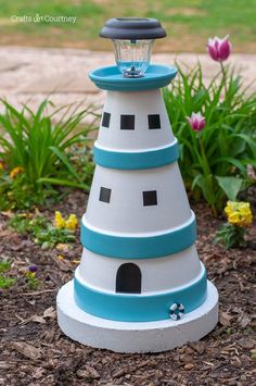 a small light house sitting in the middle of a flower bed with tulips behind it