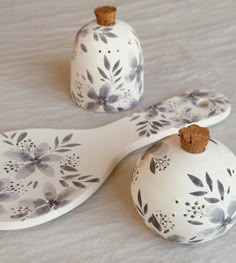 two decorative ceramic objects sitting on top of a white cloth covered tablecloth with leaves and flowers painted on them