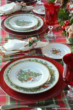 the table is set for christmas dinner with red and green plates, silverware, and napkins