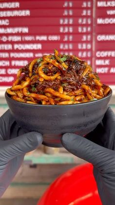 a person holding up a bowl filled with food in front of a red sign and menu