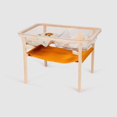 a wooden table with a glass top and yellow fabric on it, in the shape of a hammock