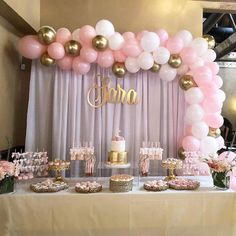 a table topped with lots of pink and white desserts next to a wall covered in balloons