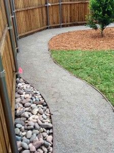 a path that is next to a fence with rocks on the bottom and grass in the middle