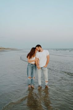 a man and woman standing in the water together at the beach with their arms around each other