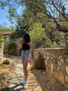 a woman walking down a dirt road next to a stone wall