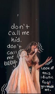 a woman in a dress singing into a microphone with words written on the wall behind her