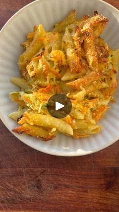 a white bowl filled with pasta and cheese on top of a wooden table next to a fork