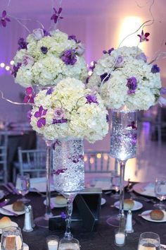 two tall vases filled with white and purple flowers on top of a black table