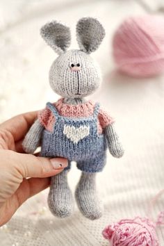 a hand holding a small knitted bunny doll in front of yarn balls and needles