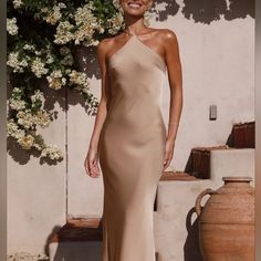 a woman standing in front of a white wall wearing a tan dress and smiling at the camera