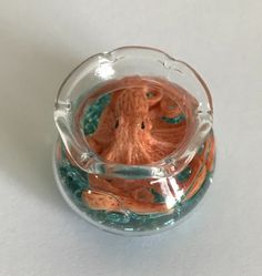 an orange octopus in a glass bowl on a white surface with blue and green bubbles