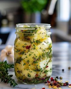 a jar filled with pickles and herbs on top of a counter next to garlic