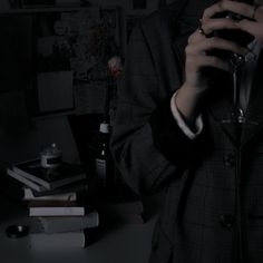 a man holding a wine glass in his hand while standing next to a desk with several books