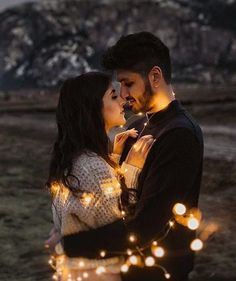 a man and woman standing next to each other with lights on their arms, in front of a mountain