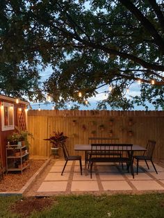 an outdoor dining area is lit up at night with string lights strung across the fence