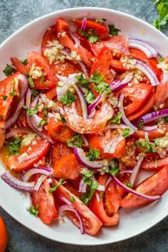 a white bowl filled with tomatoes, onions and feta cheese on top of a table