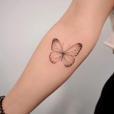 a small butterfly tattoo on the left forearm and arm, with an outline of a butterfly in black ink