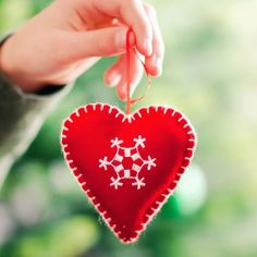 a hand holding a red heart ornament with white stars on it and string