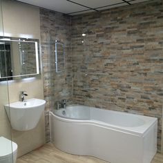 a white bath tub sitting next to a toilet under a bathroom mirror on top of a wooden floor