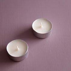 two white candles sitting next to each other on a purple surface