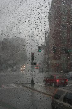 rain drops on the window as cars drive down a city street in front of traffic lights