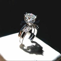 a diamond ring sitting on top of a white box in the sun with its shadow