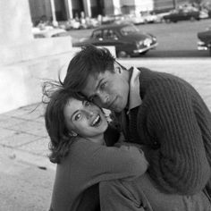 black and white photograph of two people hugging each other on the sidewalk in front of a building