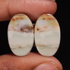 two pieces of white marble sitting on top of a persons finger in front of a black background