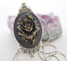 This rose necklace features a large 40x30mm oval cameo with a highly detailed rose design in black with a unique gold dry-brushed finish on a black background and secured to an antique silver plated tray with a detailed edge. Each pendant is hand painted by myself so no two are exactly alike, making this cameo very unique. This cameo pendant is strung onto a matching antique silver plated base metal snake chain that is lead and nickel free. Something unique and a touch gothic for someone special!  Oval pendant measures 40x30mm, necklace measures a length of 22 inches plus an additional 2 inches with the attached extender chain This cameo necklace will be securely wrapped and shipped for FREE anywhere in the United States in a kraft box perfect for gifting to someone special. For more of my Metal Snake, Silver Plated Trays, Gothic Gifts, Necklace Flower, Rose Pendant, Floral Pendant, Cameo Necklace, Rose Necklace, Cameo Pendant