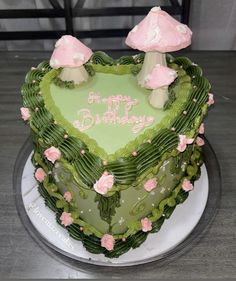 a heart shaped birthday cake with pink flowers and mushrooms on the top, sitting on a table