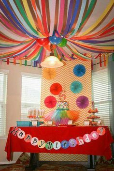 a birthday party with colorful streamers and paper umbrellas hanging from the ceiling over a table