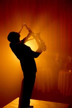 a man playing the saxophone in front of a red curtain with light coming through it