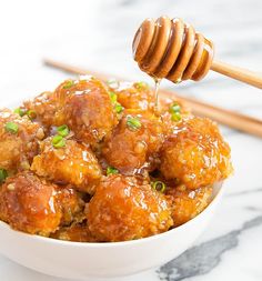 a white bowl filled with meatballs covered in sauce and topped with a honey dip