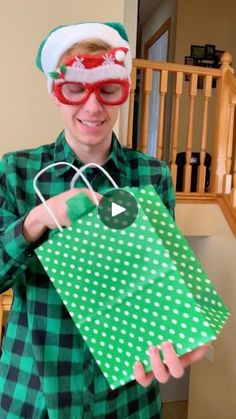 a man in plaid shirt holding up a green paper bag with santa hat on it