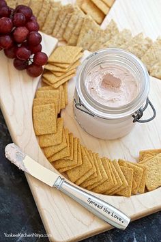 crackers and grapes are arranged on a cutting board with a jar of spread in the middle