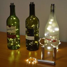 three wine bottles with lights on them sitting on a table next to a bottle opener