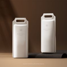 two white plastic bottles sitting on top of a black mat next to each other in front of a brown wall