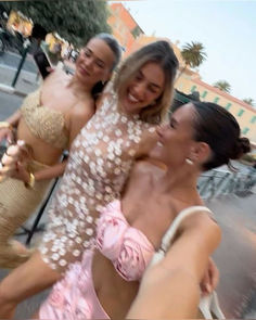 three women in bikinis are posing for a photo on the street with their arms around each other