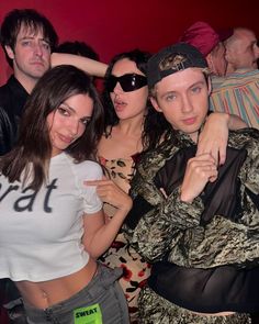 four people posing for a photo in front of a red wall with one person wearing sunglasses