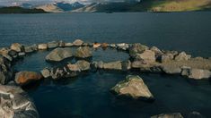 rocks are arranged in the shape of a circle near water with mountains in the background