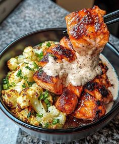 a bowl filled with chicken, cauliflower and gravy on top of a table