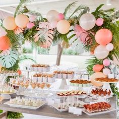 a table filled with lots of desserts under a white tent covered in palm leaves