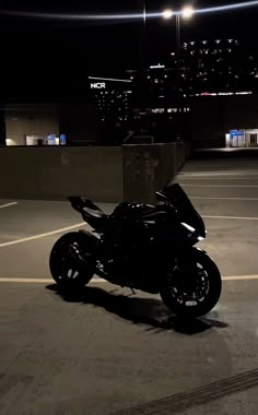 a black motorcycle parked in an empty parking lot at night with city lights behind it