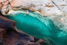 a man diving into a pool in the middle of some rocks and blue water,