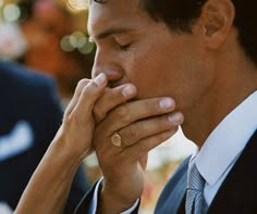 a close up of a person wearing a suit and tie holding his hands to his face