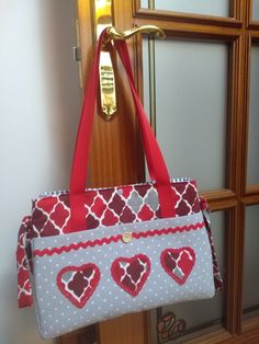 a red and white purse hanging from a door handle with hearts on the front pocket