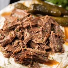 a white plate topped with mashed potatoes covered in beef and gravy next to pickles